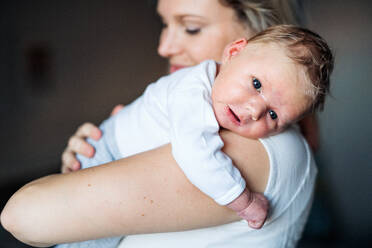 Eine schöne junge Mutter, die ihr neugeborenes Baby zu Hause im Arm hält. - HPIF24063