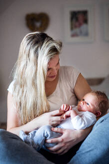 Eine schöne junge Mutter, die ihr neugeborenes Baby zu Hause im Arm hält. - HPIF24065