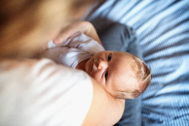 Ein Mittelteil einer nicht erkennbaren Mutter, die ein neugeborenes Baby zu Hause im Arm hält. - HPIF24070