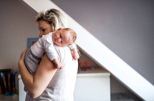 Eine schöne junge Mutter, die ihr schlafendes Neugeborenes zu Hause im Arm hält. Platz kopieren. - HPIF24076