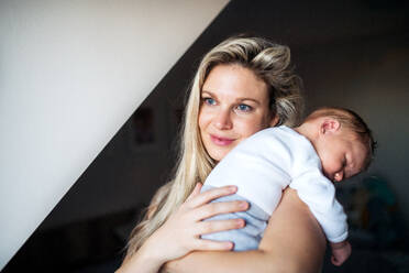 Eine schöne junge Mutter, die ihr schlafendes Neugeborenes zu Hause im Arm hält. Platz kopieren. - HPIF24078