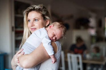 Eine schöne junge Mutter, die ihr schlafendes Neugeborenes zu Hause im Arm hält. Platz kopieren. - HPIF24079