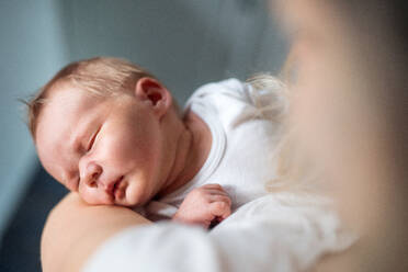 Eine Nahaufnahme einer nicht erkennbaren Mutter, die ein schlafendes Neugeborenes zu Hause im Arm hält. - HPIF24080