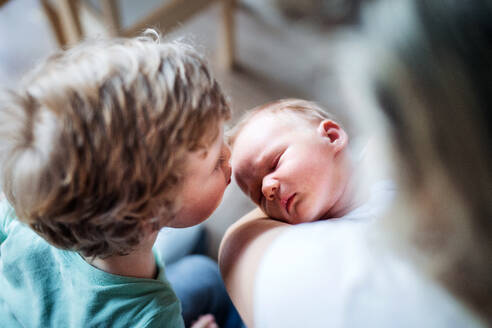 Ein kleiner Junge küsst zu Hause sein schlafendes neugeborenes Brüderchen, die Mutter hält es im Arm. - HPIF24081