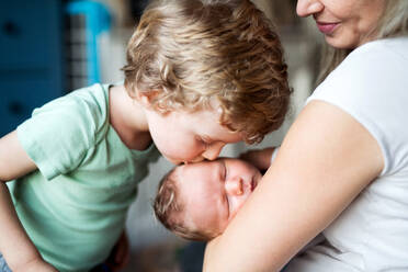 A small boy kissing a sleeping newborn baby brother at home, a mother holding him. - HPIF24082