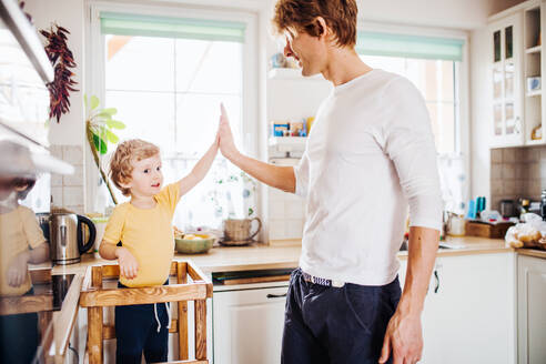 Ein junger Vater mit einem kleinen Sohn, der zu Hause in der Küche Zeit verbringt, gibt High Five. - HPIF24095