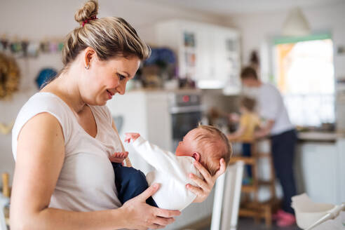 Eine schöne junge Mutter hält ein neugeborenes Baby in der Küche zu Hause. - HPIF24096