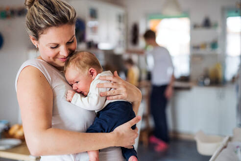 Eine schöne junge Mutter, die ihr neugeborenes Baby zu Hause im Arm hält. - HPIF24097