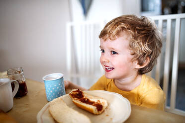 A front view of a happy toddler boy sitting at the table at home, eating. - HPIF24102