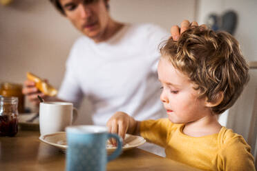 A young father with a toddler son eating breakfast indoors at home. - HPIF24107