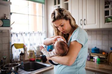 Eine schöne junge Mutter, die ihr neugeborenes Baby zu Hause im Arm hält. - HPIF24108