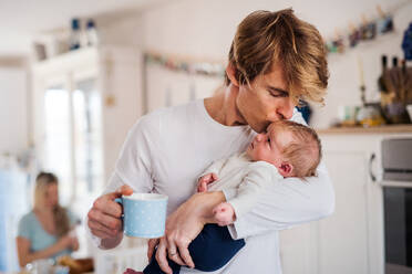 A young father holding a newborn baby in kitchen at home, kissing. - HPIF24112