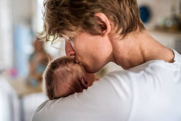 Nahaufnahme eines jungen Vaters, der sein neugeborenes Baby zu Hause im Arm hält und es küsst. - HPIF24115