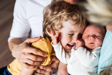 A midsection of father with newborn baby and small toddler son at home. - HPIF24128