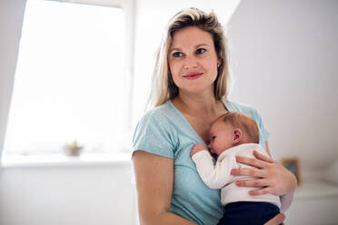 Eine schöne junge Mutter, die ihr neugeborenes Baby zu Hause im Arm hält. - HPIF24136