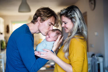 Beautiful young parents holding a newborn baby at home, kissing. - HPIF24146