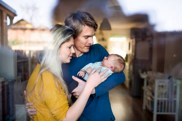 Schöne junge Eltern, die ein neugeborenes Baby zu Hause im Arm halten, aufgenommen durch Glas. - HPIF24150
