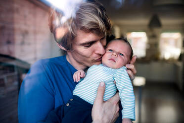 Ein junger Vater hält sein neugeborenes Baby zu Hause im Arm und küsst es, aufgenommen durch Glas. - HPIF24151