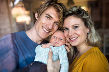 Beautiful young parents holding a newborn baby at home. Shot through glass. - HPIF24153
