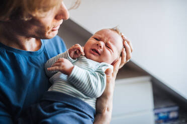 Nahaufnahme eines jungen Vaters, der ein weinendes Neugeborenes zu Hause hält. - HPIF24161