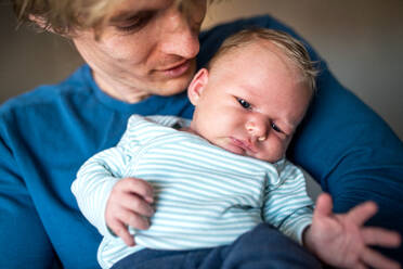 Nahaufnahme eines jungen Vaters, der ein neugeborenes Baby zu Hause im Arm hält, Vorderansicht. - HPIF24163
