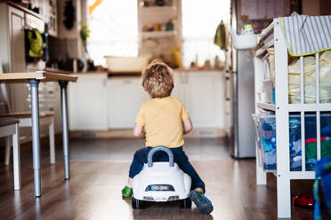 Rückansicht eines Kleinkindes mit Spielzeugauto, das in der Küche zu Hause spielt. - HPIF24170