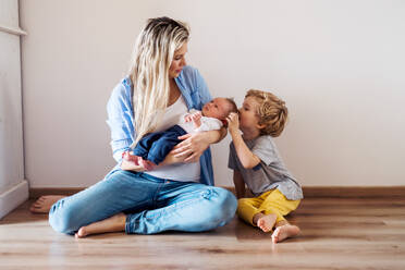 Eine schöne junge Mutter mit einem neugeborenen Baby und seinem kleinen Bruder zu Hause. - HPIF24184