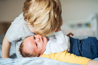 A small toddler boy sitting a newborn baby brother at home, sitting on bed. - HPIF24190