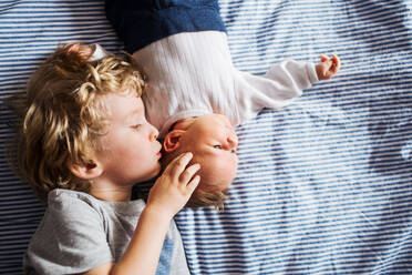 A top view of small toddler boy with a newborn baby brother at home, lying down on bed. - HPIF24194