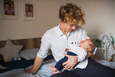 Ein glücklicher junger Vater mit einem neugeborenen Sohn, der zu Hause im Bett sitzt. - HPIF24195