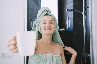 Smiling woman holding coffee mug outside bathroom - NDEF00617