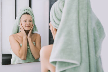 Lächelnde Frau trägt Gesichtscreme auf und schaut in den Spiegel - NDEF00619