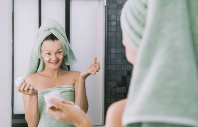 Smiling woman applying cream on face after shower - NDEF00621