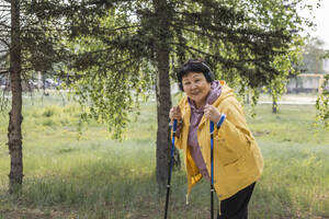 Lächelnde ältere Frau mit Spazierstöcken im Park - ADF00099