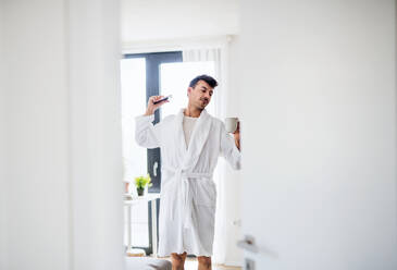 Junger Mann mit Kaffee und Smartphone im Schlafzimmer am Morgen, Stretching. - HPIF24223