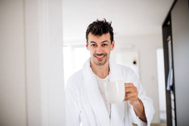 Front view of young man with coffee in the bedroom in the morning. - HPIF24226