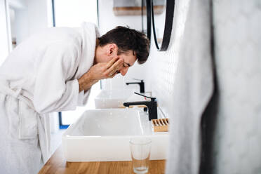 Ein junger Mann wäscht sich morgens im Badezimmer das Gesicht, eine tägliche Routine. - HPIF24228