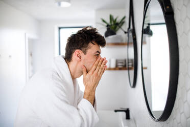 Young man washing face in the bathroom in the morning, a daily routine. - HPIF24229