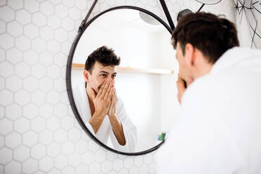 A young man looking in mirror in the bathroom in the morning, daily routine. - HPIF24230