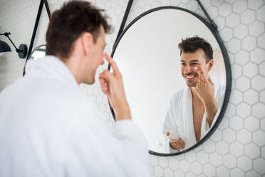 Young man putting cream on face in the bathroom in the morning, a daily routine. - HPIF24252