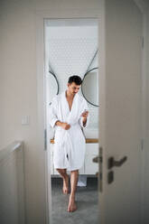 Ein junger Mann steht morgens im Badezimmer und benutzt sein Smartphone. - HPIF24255