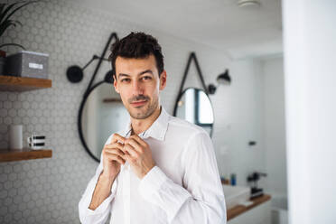 A young man putting on shirt in the bathroom in the morning. - HPIF24261