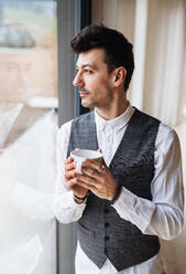 Ein junger Mann mit Kaffee, der am Fenster steht. Raum kopieren. - HPIF24301