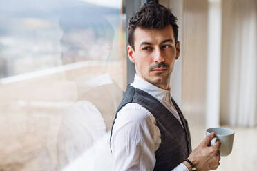 A young man with coffee standing by the window. Copy space. - HPIF24302