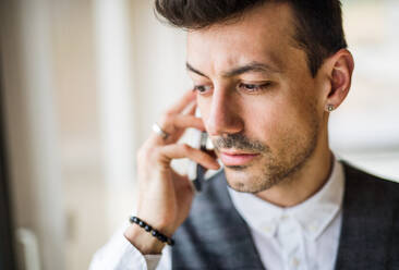 A young man with smartphone standing indoors at home, making a phone call. - HPIF24305