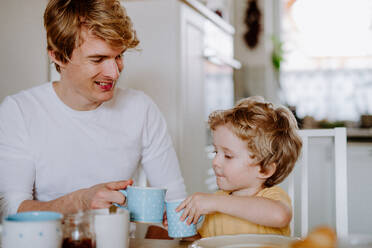 Ein junger Vater mit einem kleinen Sohn frühstückt zu Hause. - HPIF24312