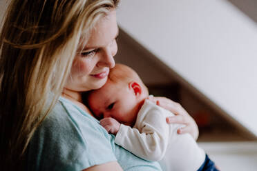 Eine schöne junge Mutter, die ihr neugeborenes Baby zu Hause im Arm hält. - HPIF24317