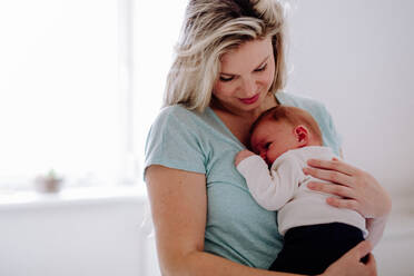 Eine schöne junge Mutter, die ihr neugeborenes Baby zu Hause im Arm hält. - HPIF24319