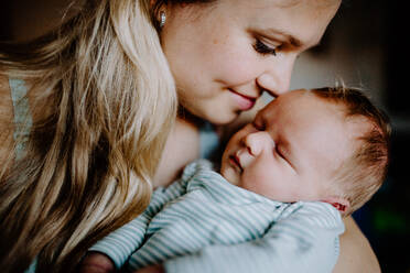 Eine schöne junge Mutter, die ihr neugeborenes Baby zu Hause im Arm hält. - HPIF24323