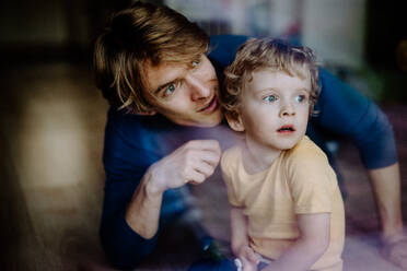 Ein glücklicher Vater, der seinen kleinen Sohn zu Hause im Arm hält, fotografiert durch Glas. - HPIF24327